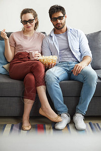 现代夫妇坐在沙发上坐在一起看电视在家穿着太阳眼镜图片