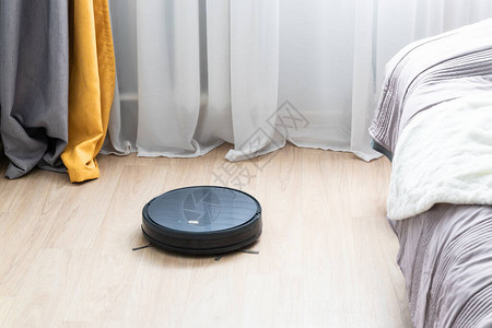 黑色塑料圆形机器人真空吸尘器清洁工通过客厅的Wifi远程清理光地板智能家背景图片