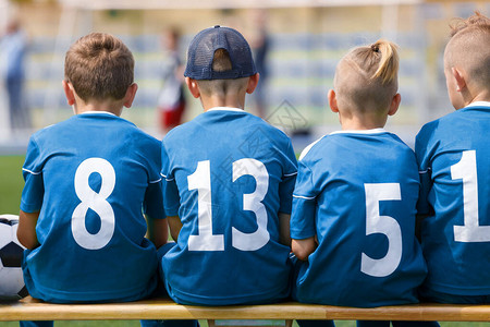 运动队的快乐男孩子们在木凳上的足球运动员背景中的儿图片