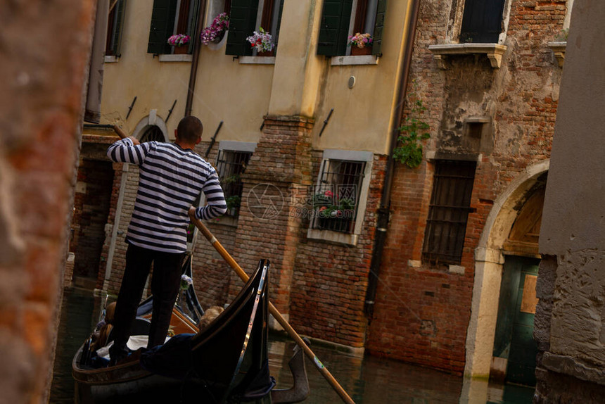 一个Gondolier人骑着游客穿过威尼斯秋天狭窄的运河图片