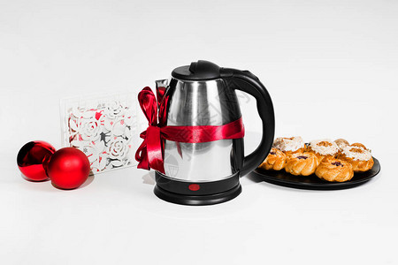 白色背景上的礼品丝带中的电热水壶茶壶与桌上的纸杯蛋糕家用小家电图片