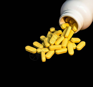 黄色维生素C药片喷洒和深底的白药瓶选择焦点图片