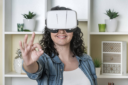 戴尼姆夹克和VR护目镜中的正成年女士在留家中探索虚拟现实时微笑并图片