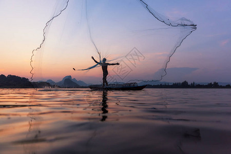亚洲渔民在黄昏时分在湖边的木船上投掷渔网农村渔民生活方式的概念华富里图片