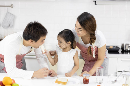 快乐的亚洲家庭做饭父亲母亲和女儿正在家里的厨房里吃早餐面包加果酱图片