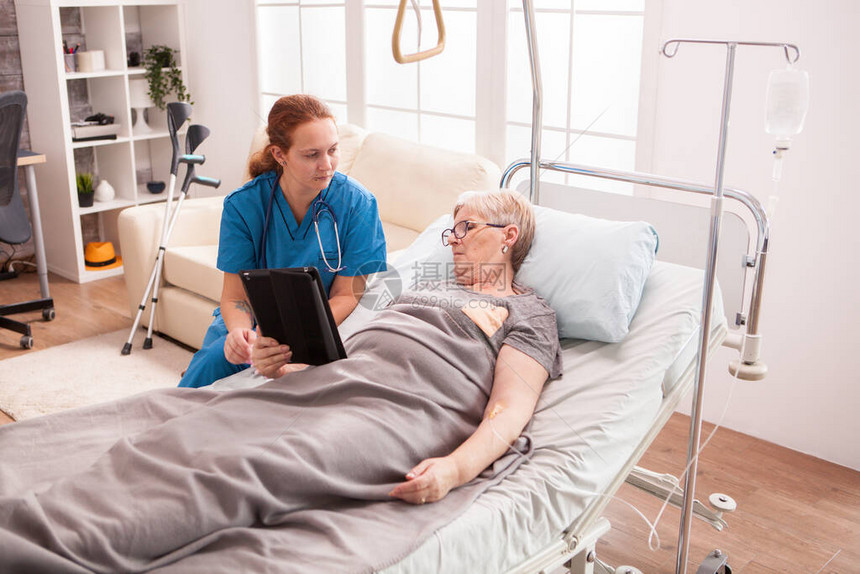 疗养院的女医生坐在高龄妇女旁边用平板图片