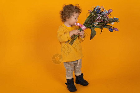 带花的小男孩可爱的卷发小男孩手里拿着一束五颜六色的郁金香黄色背景节日图片