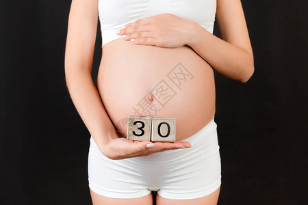 关闭穿着白色内衣的孕妇拿着带有怀孕周数的立方体在黑色背景下怀孕三十图片