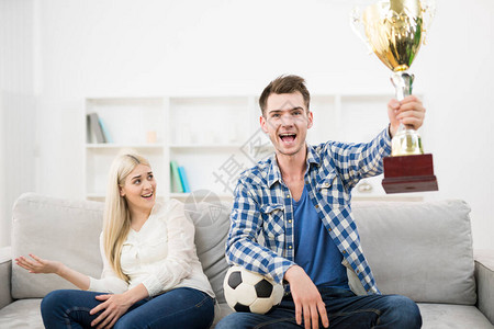 快乐的男子看着橄榄球在沙发上靠图片