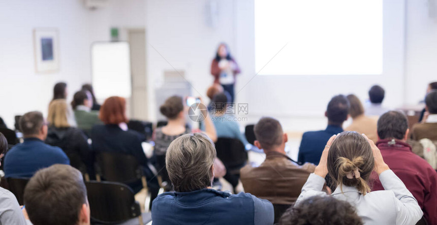 商业和创业研讨会女发言人在商务会议上发表演讲会议厅内的观众观众中未被识别的参与者的后视图在白图片