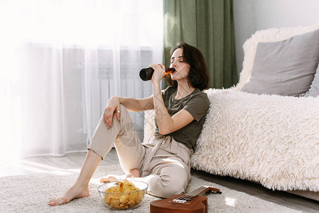 一个年轻女人在家里喝啤酒吃薯片在家看电视和电影图片