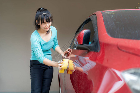 亚裔女在家中用肥皂和海绵为家用洗涤车主的红色轿车感到快乐图片
