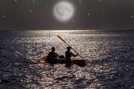 晚上在大月光照耀的海面上骑着皮艇的年轻夫妇图片