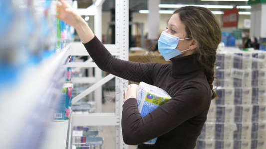 一名戴医疗面具的年轻女子在超市田地上捡起许多卫生纸包背景图片