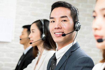 微笑的亚洲男客户服务电话营销代理与他的团队在图片
