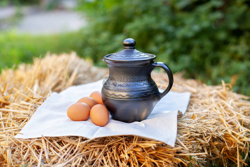 泥壶和鸡蛋在花园里的稻草上泥壶里的牛奶有机产品概念天然产品图片