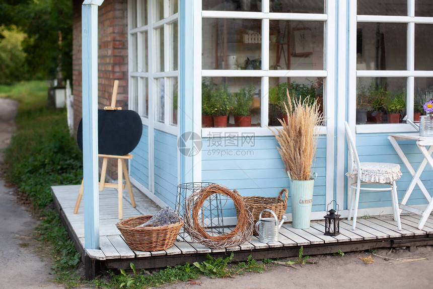 园艺工具旁边的柳条筐喷壶和干小穗蒲苇靠在蓝房子的墙上园艺概念收获乡间别墅院子的舒适装图片