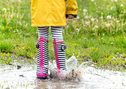 一个穿着橡胶靴的孩子在水坑里跳特写秋夏概念图片