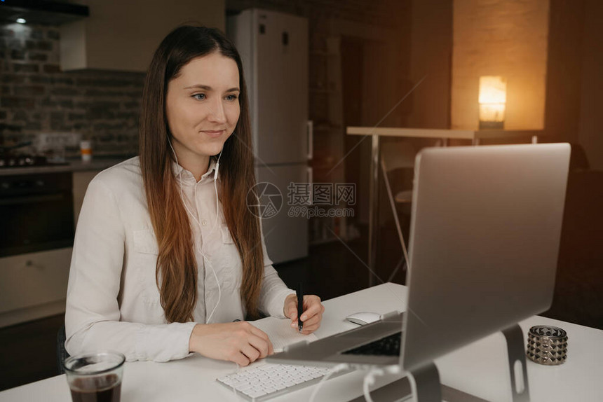 远程工作一位戴着耳机在笔记本电脑上远程工作的白人女一个穿着白衬衫的黑发女孩在她舒适的家庭工作场所的在线商务图片