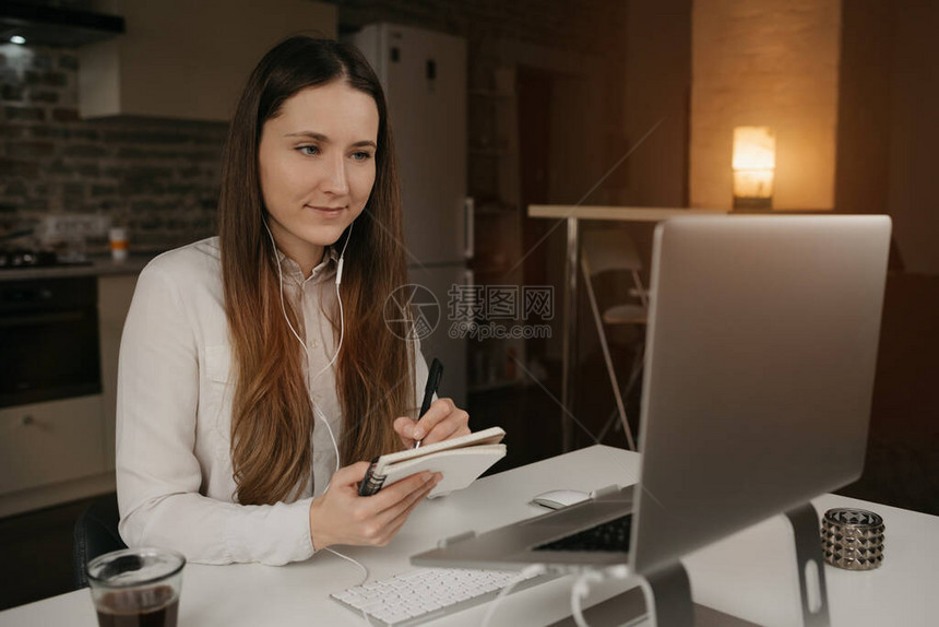 远程工作一位戴着耳机在笔记本电脑上远程工作的白人女一个穿着白衬衫的女孩在她舒适的家庭工作场所的在线商务图片