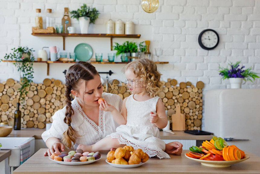 一个快乐的母亲和女儿的家族肖像在早餐时在厨房里摆着吃了美味的马卡龙饼图片