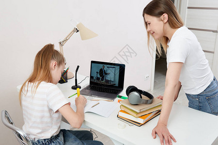 母亲观看她女儿在家用笔记本电脑做家庭作业图片
