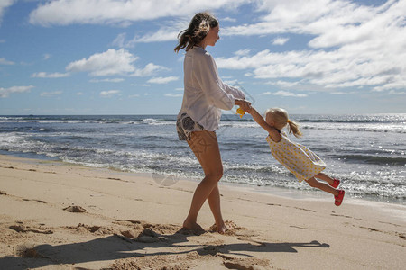 母亲和她蹒跚学步的小女孩在海滩享受一天快乐的图片