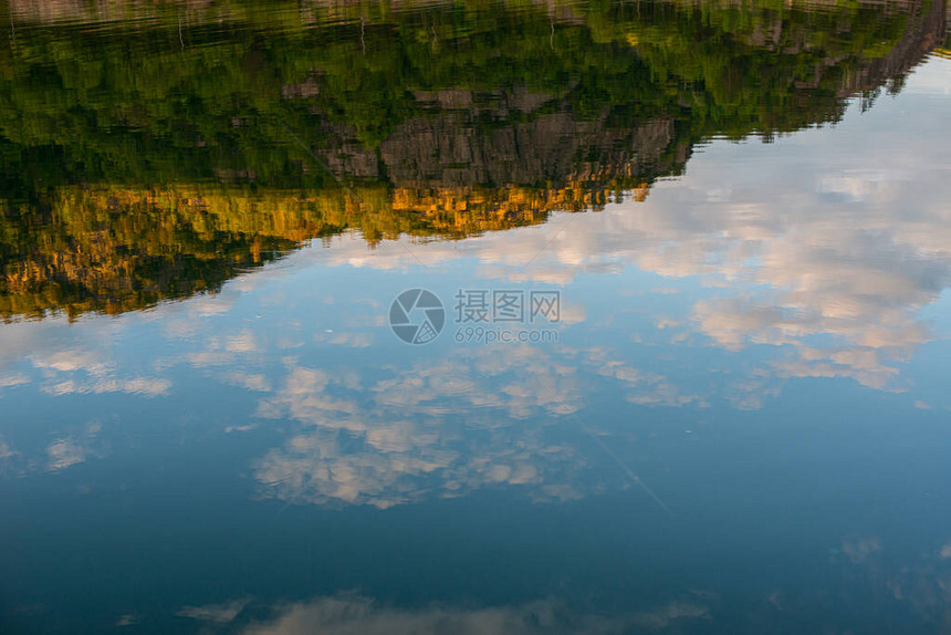 森林小山和湖中多云天空的倒影图片