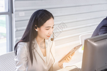 亚洲女呼叫中心运营商观看发光的数字平板电脑背景图片