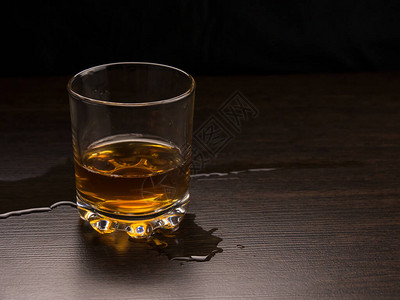 一杯威士忌和溢出的液体放在黑暗的木板上图片