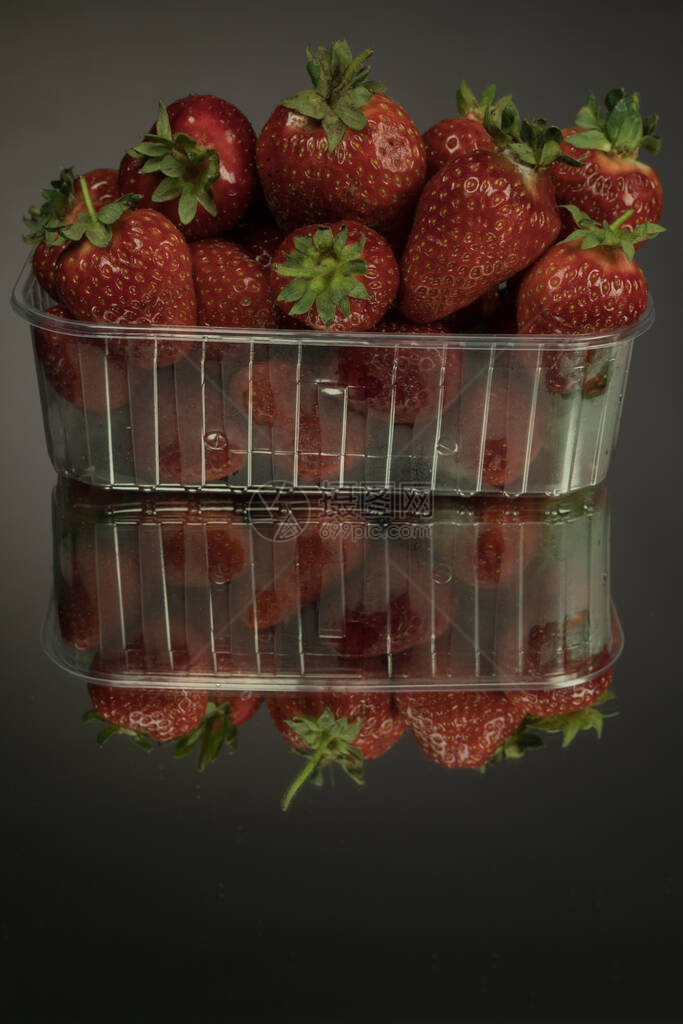 新鲜草莓装在透明塑料盒中在镜面黑色背景上草莓富含维生素微量元图片