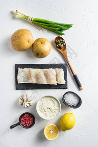 传统的鱼和薯条配料方在石板面糊土豆鞑靼酱薄荷糊状豌豆柠檬葱薄荷大蒜盐胡椒粒上的生鳕鱼片背景图片
