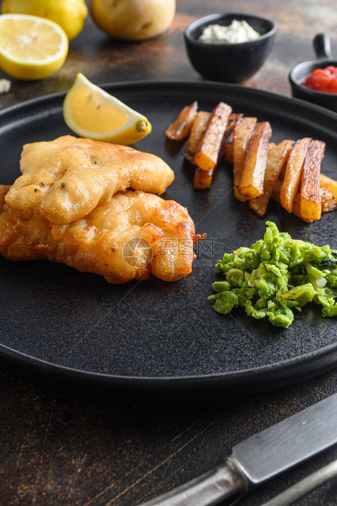 英国传统鱼和薯条配薄荷豌豆泥鞑靼酱在黑盘上的垂直侧视图特写细节侧视图在旧的仿图片