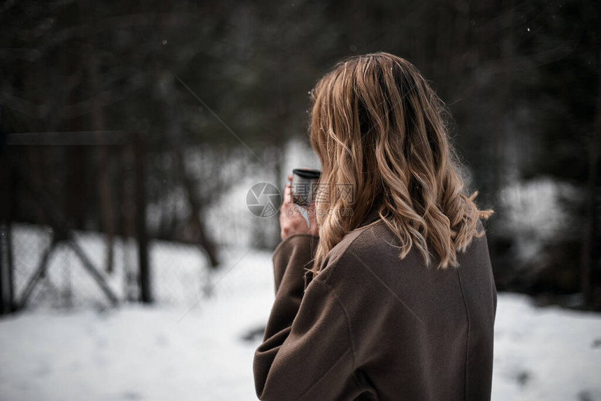 金发女孩在冬天的森林里喝热水从热温杯图片