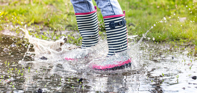 一个穿着橡胶靴的孩子在水坑里跳特写秋夏概念图片