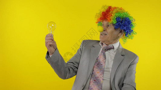 戴假发和商务西装的高级小丑办公室工人展示灯泡图片