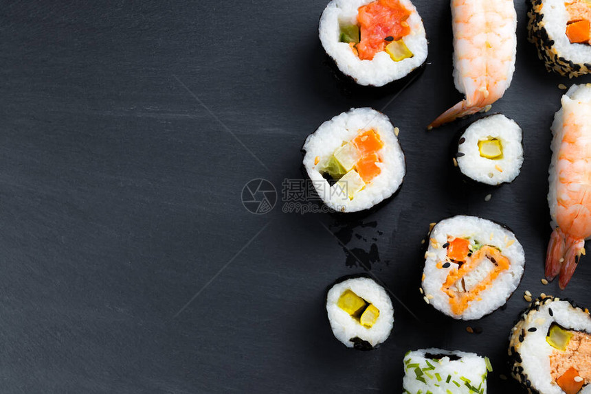 典型的亚洲美食设置在黑色厨房石板上寿司futomaki和握寿司生鱼片配米饭和蔬菜复图片