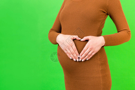 种植孕妇在绿背景下用手抚摸腹部塑造心形的画面婴儿碰撞概念复制空图片