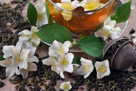 茉莉花绿茶干绿茶叶与茉莉花和木桌上的图片