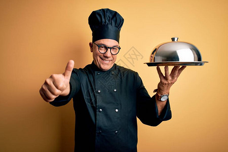 中年时英俊的灰发服务员男子身着厨师制服和帽子托盘图片