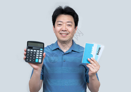 一个亚洲中年男子手握着一张银行存折和计算器图片