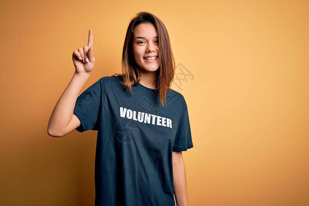 年轻漂亮的黑发女孩做志愿者穿着t恤与志愿者信息词用成功的想法指点退出图片