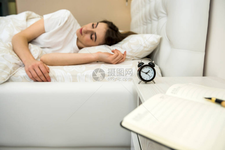 桌子上的闹钟和妇女睡在背景中保健与睡眠图片