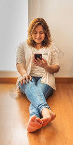 女人戴着手机坐在家里窗户旁边的地板上女人在视图片