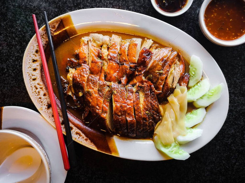 烤鸭片或北京烤鸭片在白盘上用筷子和辣酱在深色背景上的顶部视图图片