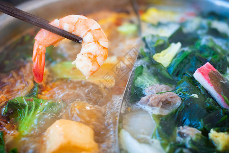 在双口味的热锅上紧握着虾子的竹筷子还有肉类海鲜药草背景图片