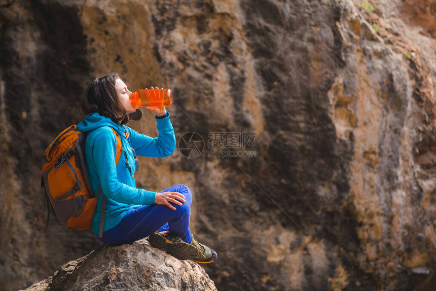 一个背着包的女人从一个可重复使用的瓶子里喝水一个女孩坐在一块大石头上解渴岩石背图片