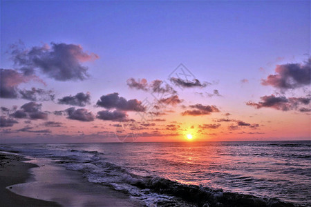 加勒比海的美妙日出刚从地平线升起云和天空被描绘成令人难以置信的猩红色粉红色橙色紫色紫罗兰色蓝色调小浪滚到沙滩上水上阳背景图片