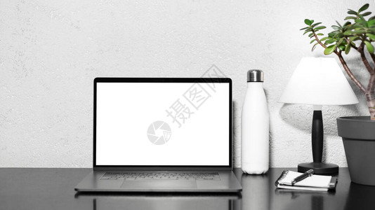 自由职业者工作场所在钢制热水瓶灯花和带笔的记本旁边的黑色桌子上带样机的笔记本电脑背景图片