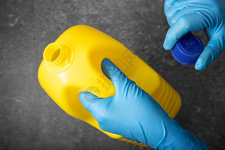 戴着黄色漂白剂瓶的防护手套中的人体手图片